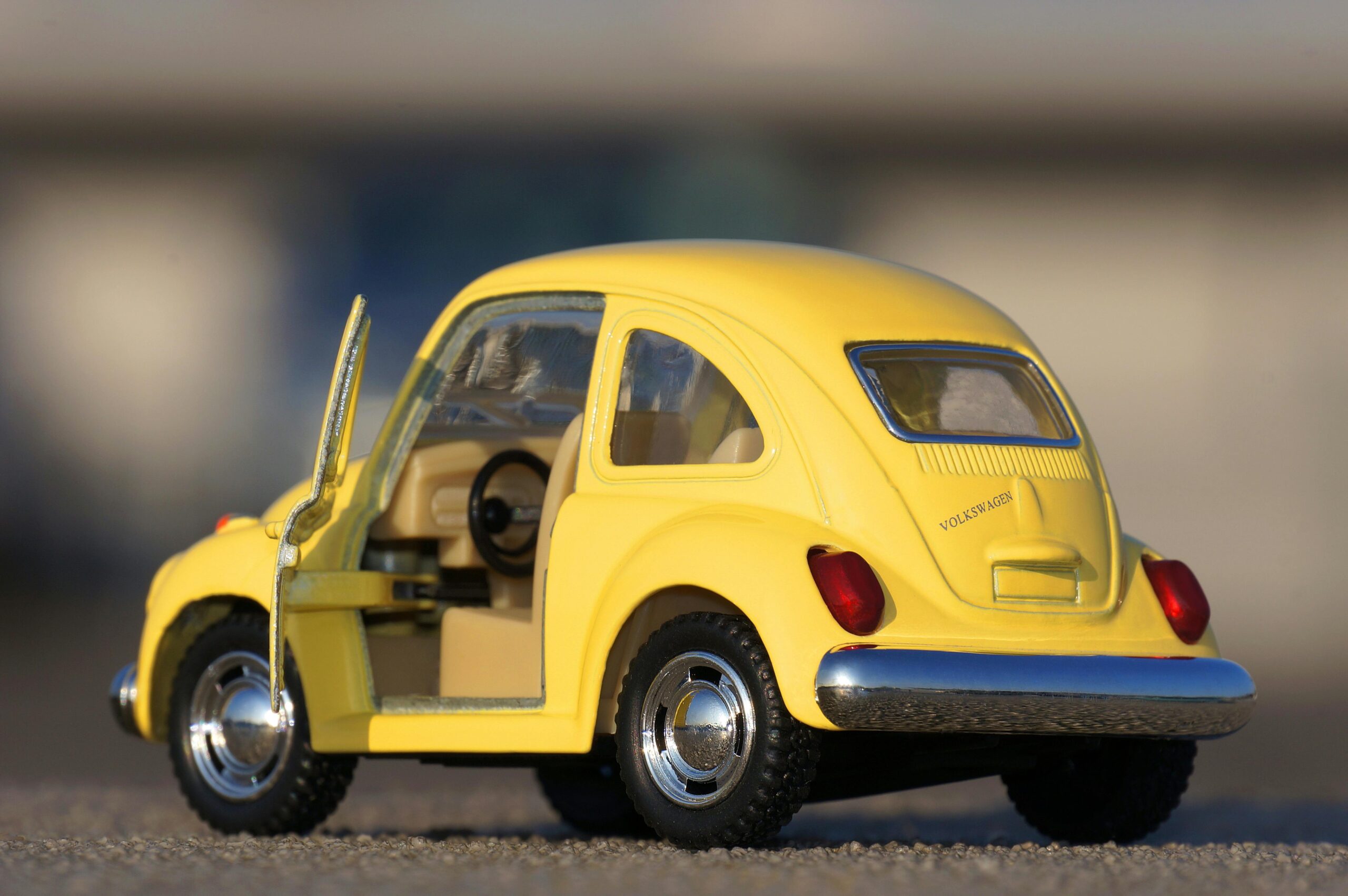 Detailed close-up of a yellow miniature Volkswagen Beetle toy car on pavement.